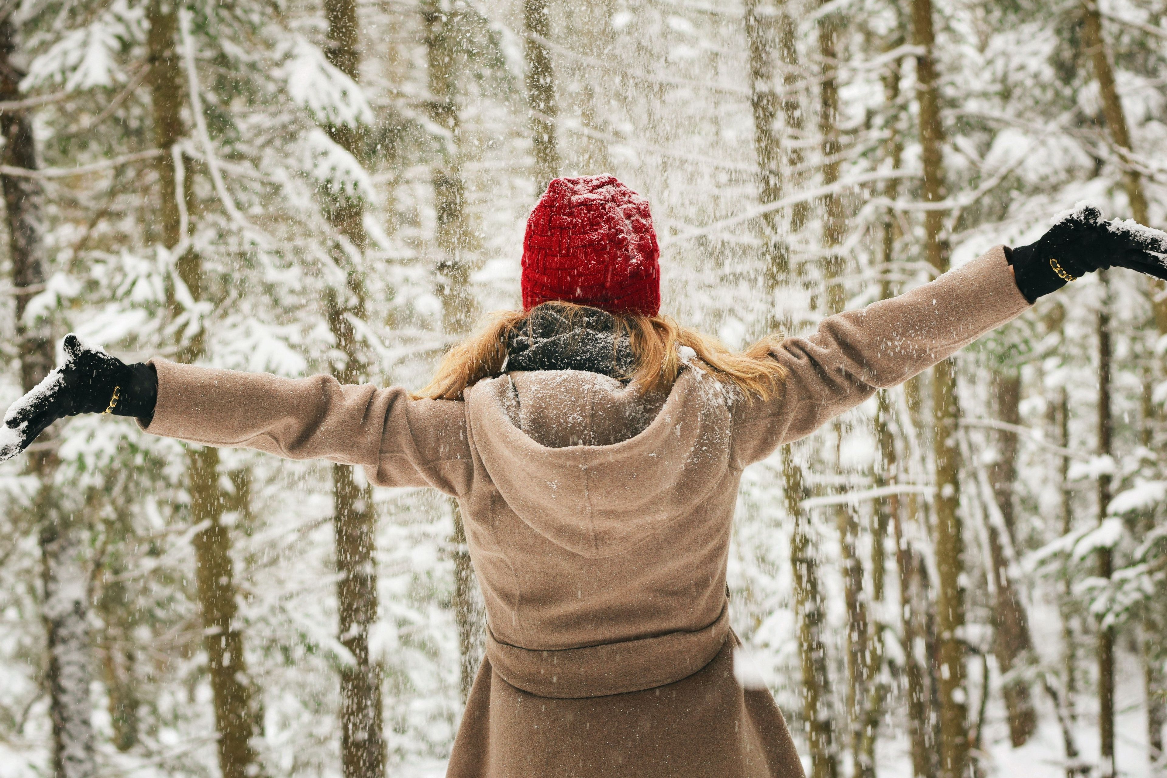 Woman with arms stretched out looking at snowy woods 